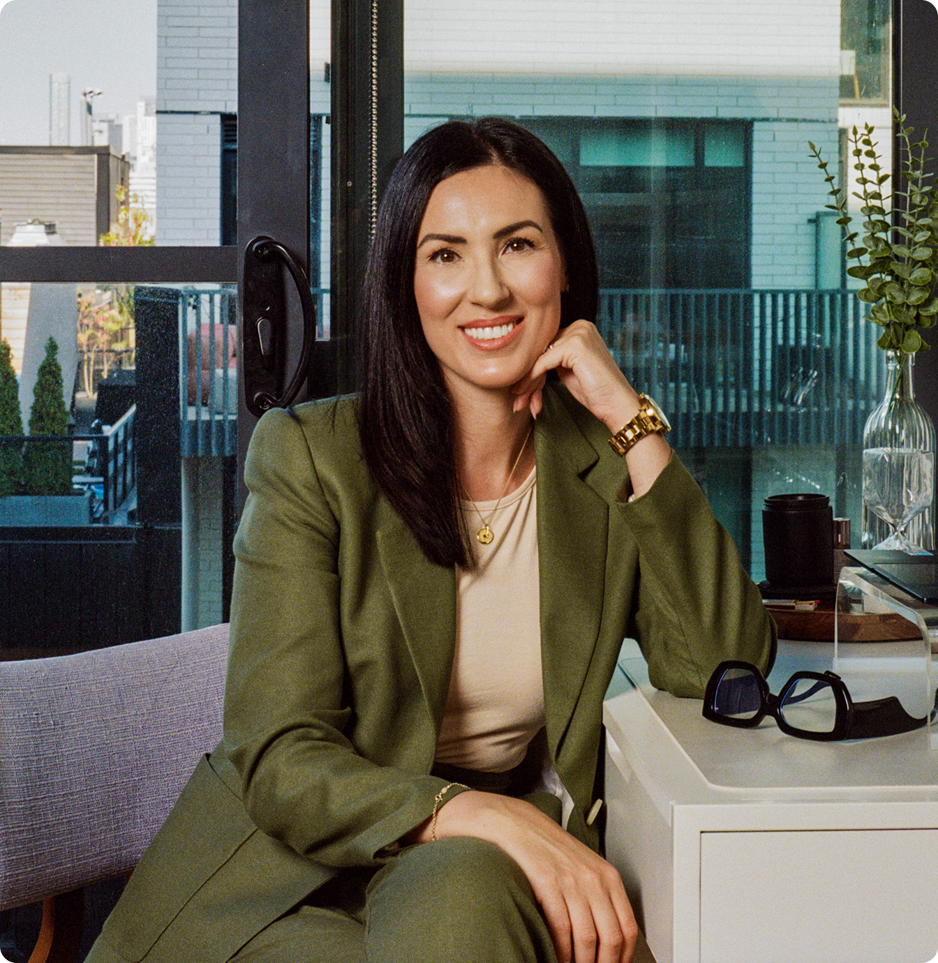 Confident businesswoman in a green suit smiling while seated in a modern office space.