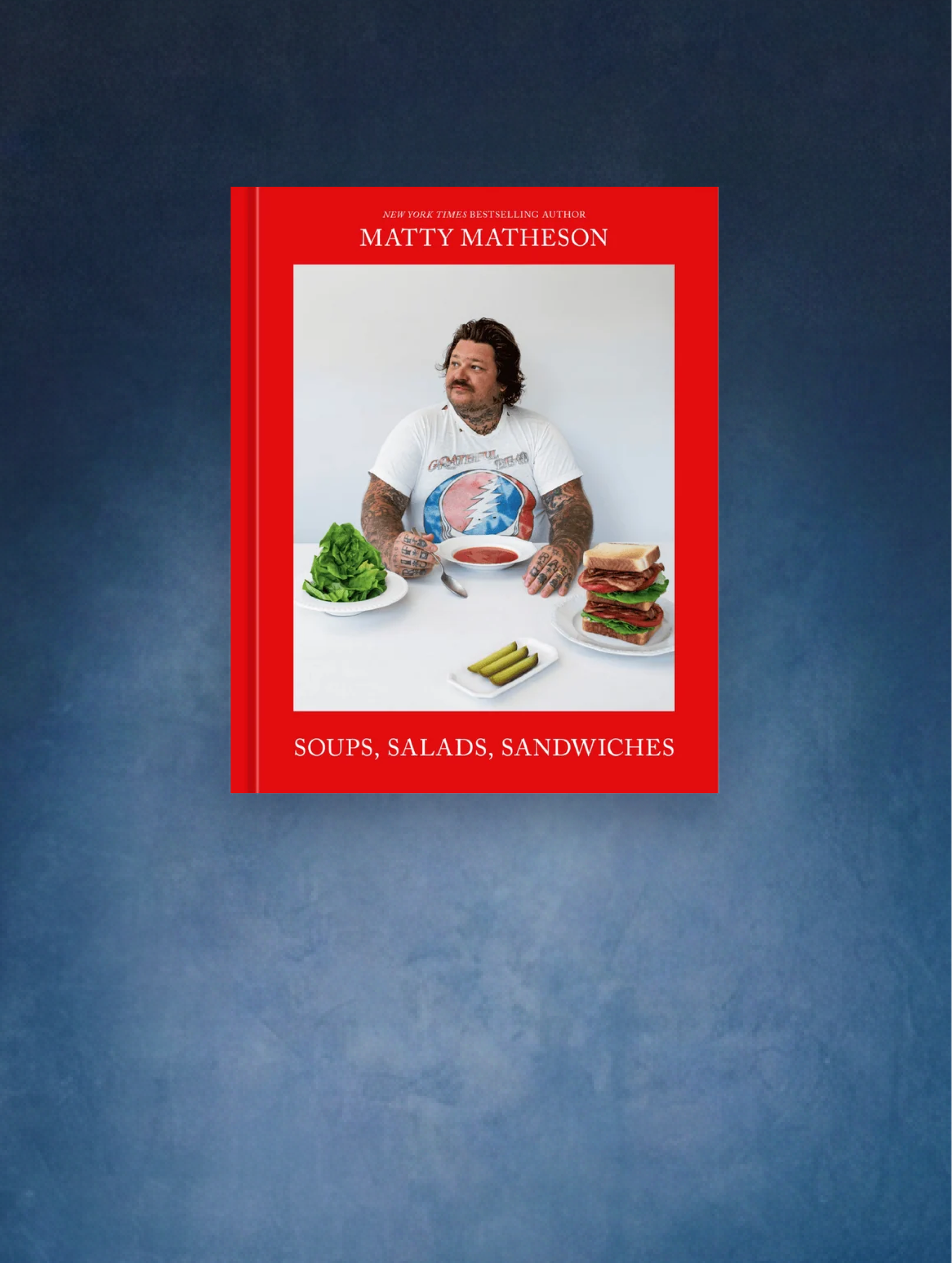 Un livre de cuisine rouge vif de Matty Matheson. Sur la couverture, une photo de Marie Matheson attablée devant une salade, une soupe, un sandwich et une assiette de cornichons.
